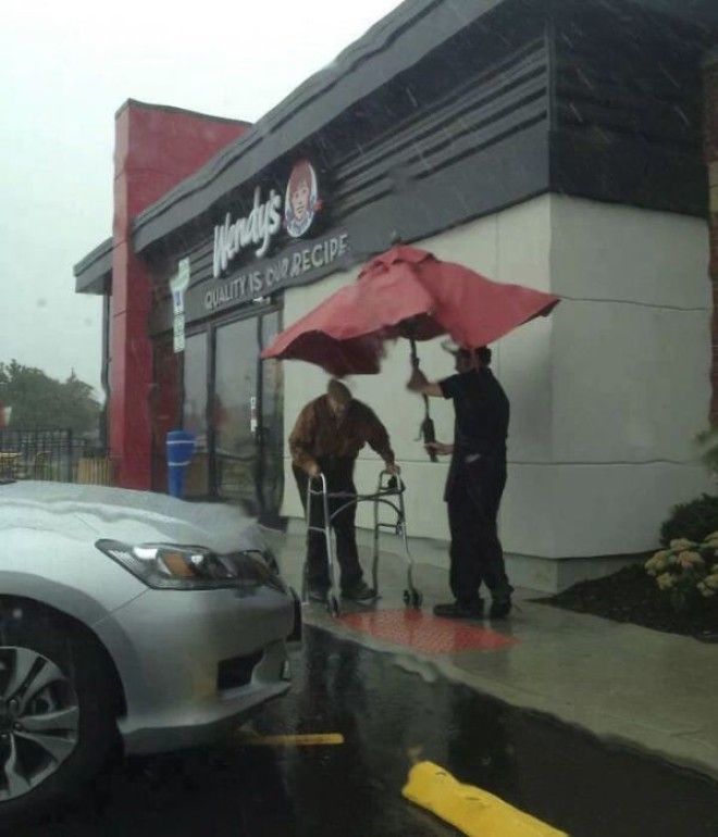 Сотрудники магазина вынесли зонтик со стола на улицу чтобы помочь пожилому мужчине пройти под дождем к машине